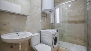 Une salle de bain équipée d’un lavabo, de toilettes, d’un lave-linge et d’une douche à parois en verre.