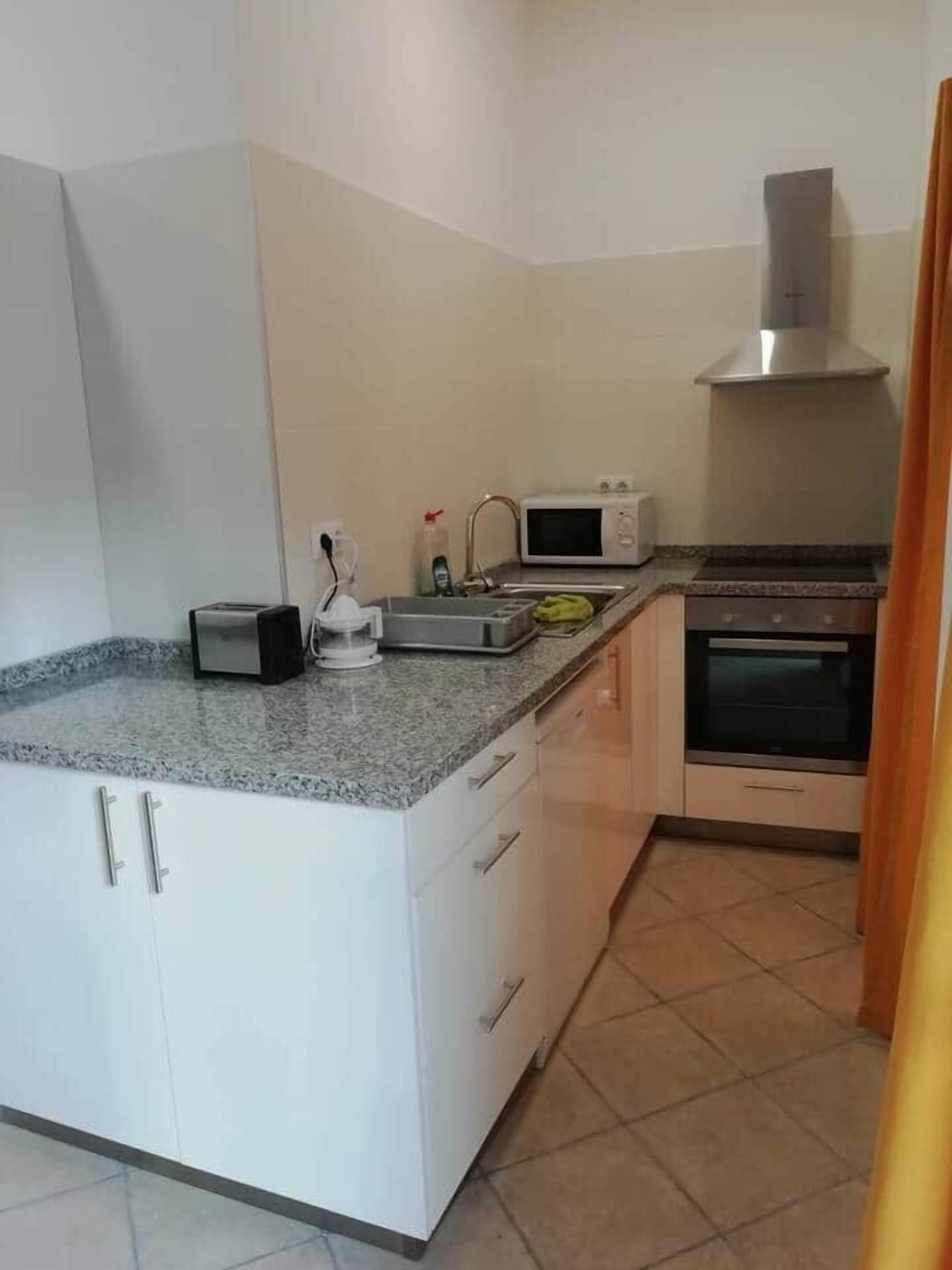 Una cocina con armarios blancos, microondas, tostadora y horno.