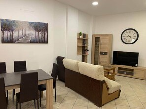 Ein Wohnzimmer mit einer Couch, Fernseher, Holzschrank und einem Bild an der Wand.