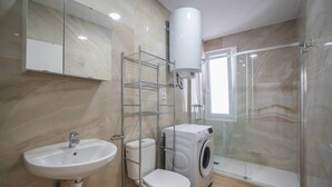 Een badkamer met een wastafel, toilet, wasmachine en een douchecabine.
