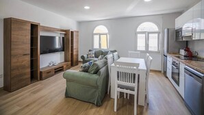 Een moderne woonkamer met een televisie, bank, eettafel en een keukenhoek.