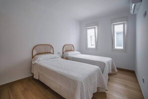 Une chambre avec deux lits simples, des têtes de lit en bois, du linge de lit blanc et deux fenêtres.