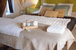 A neatly made bed with a white towel, a tray of candles, and a small bowl of oil. - L'Écurie Vacation Rental (Wierre-Effroy)