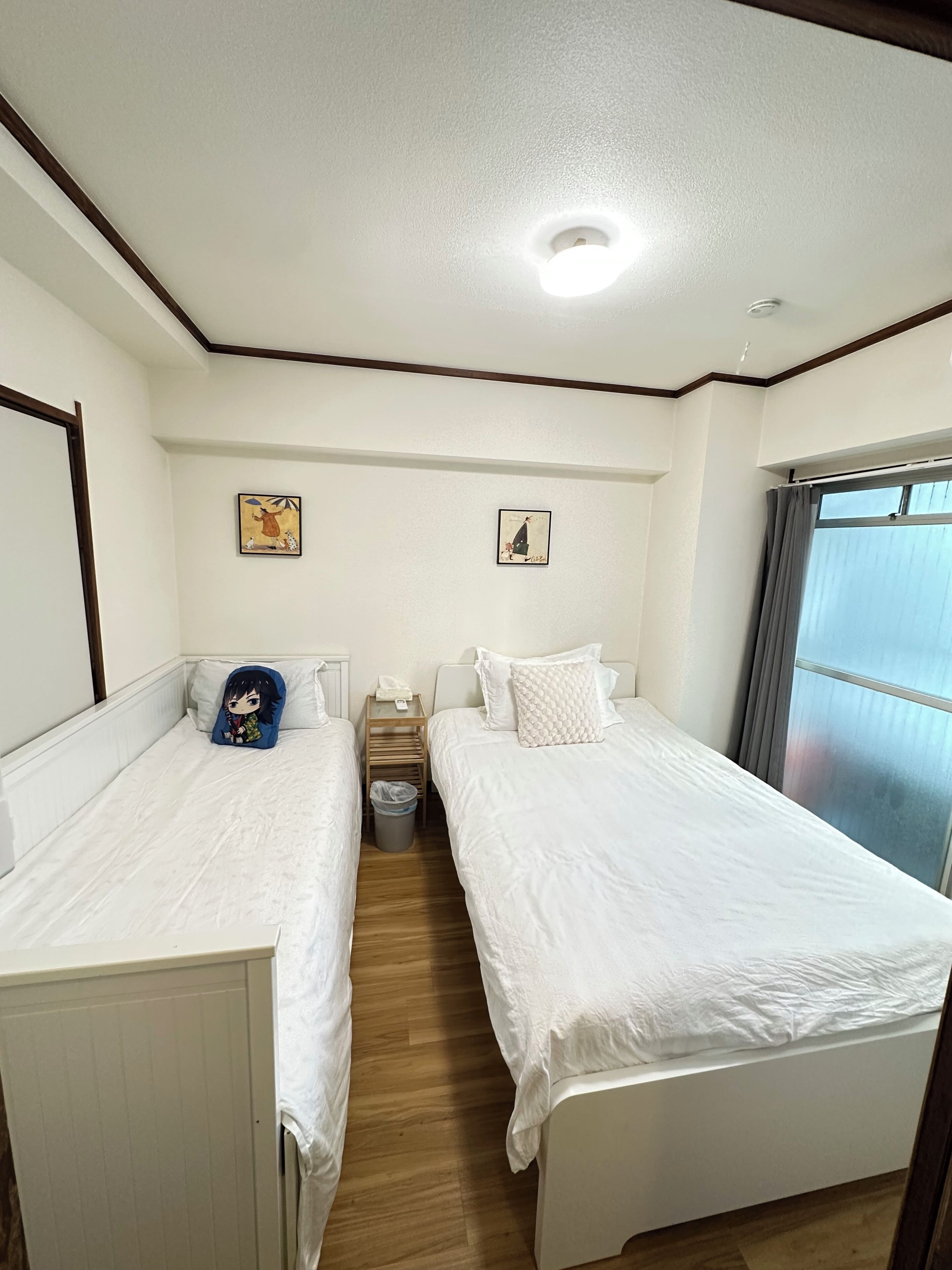 Une chambre avec deux lits, un plancher en bois, un luminaire au plafond et une fenêtre avec des rideaux.