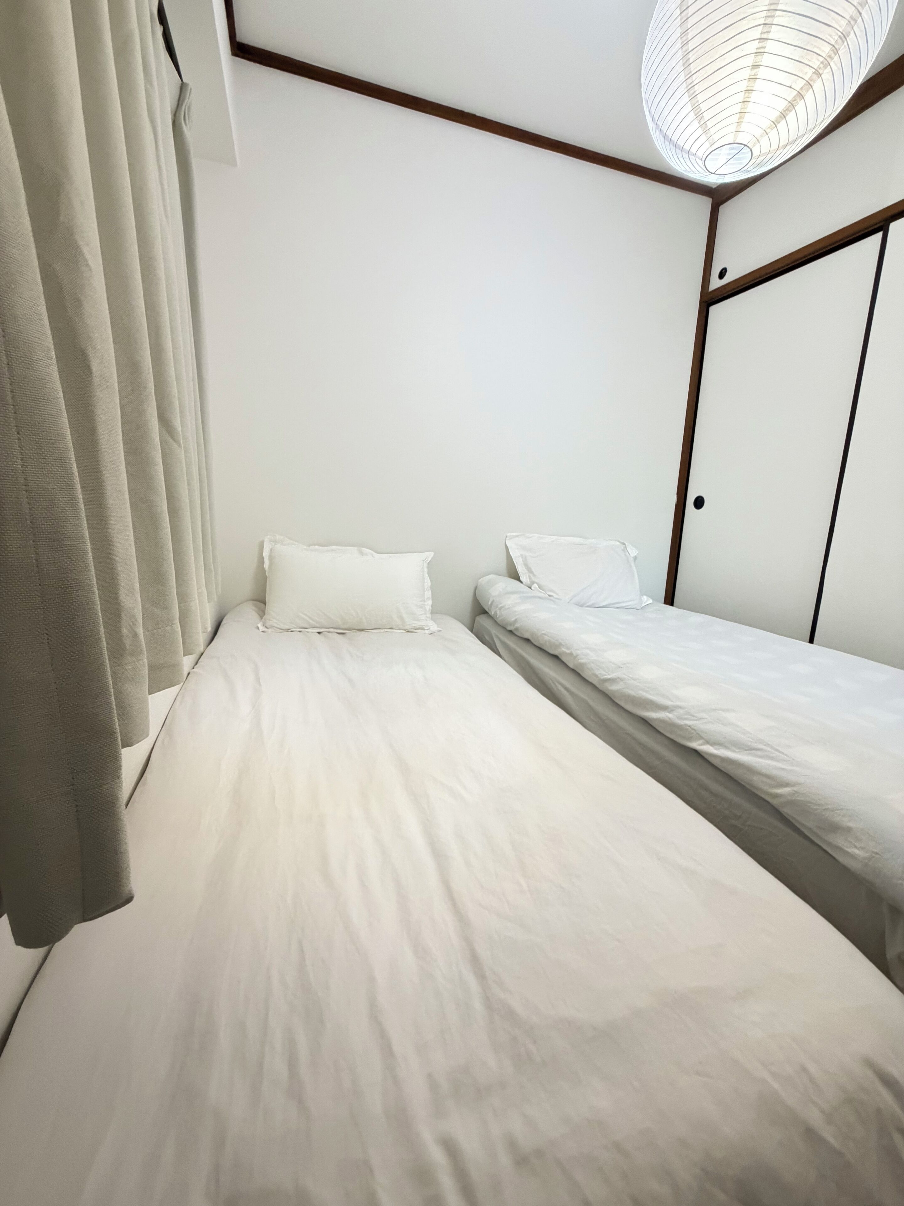 A room with two beds, a ceiling light fixture, and a door.