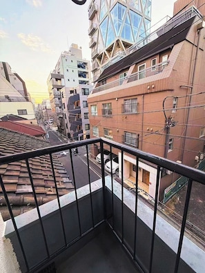 Un balcon donnant sur une rue de la ville, avec vue sur des immeubles et une structure moderne en verre.