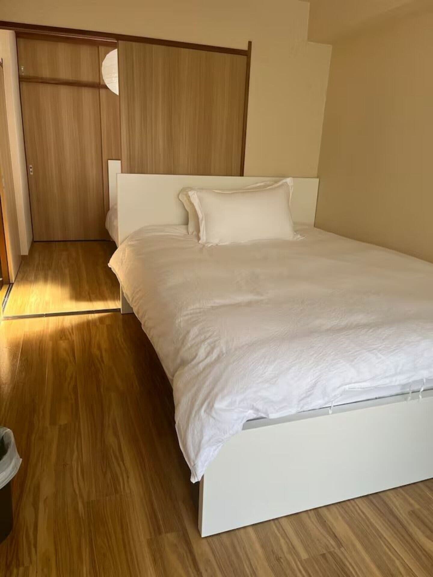 Une chambre avec un lit simple, un plancher en bois, un lit blanc et une armoire en bois.