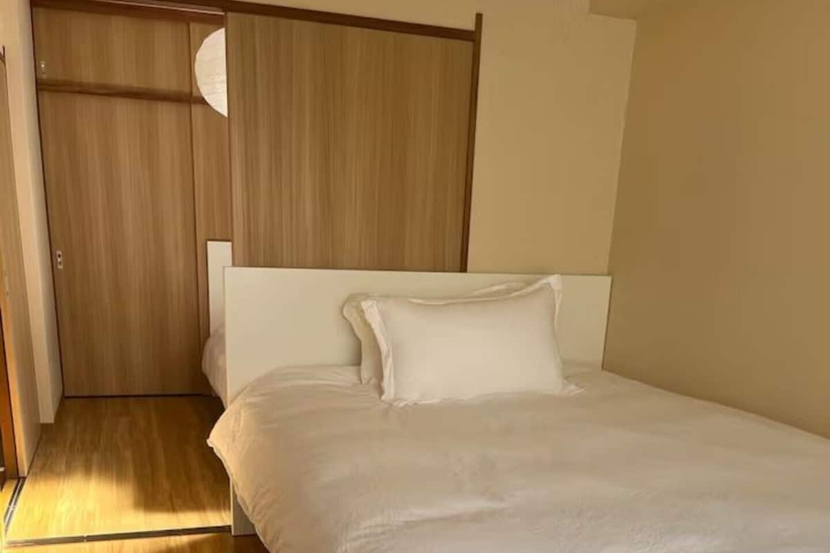 Une chambre avec un lit simple, un plancher en bois, un lit blanc et une armoire en bois.