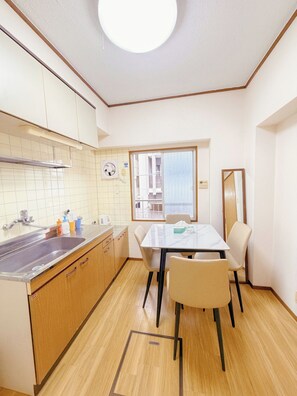 A compact kitchen with a sink, cabinets, and a dining area with chairs. - sannritsu (Tokyo)