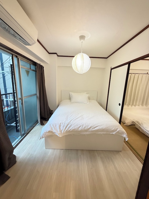 Une chambre avec un grand lit, un luminaire au plafond et une porte-fenêtre coulissante sur le côté gauche.