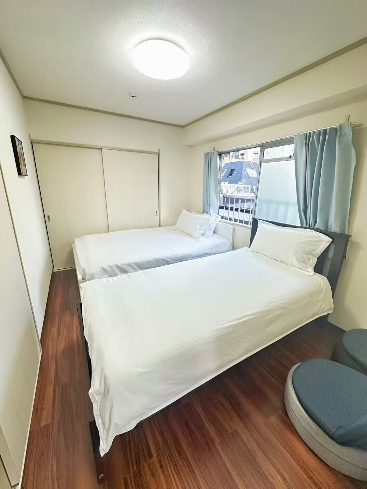 Une chambre avec deux lits, une fenêtre avec des rideaux, une porte et une vue sur les bâtiments à l’extérieur.