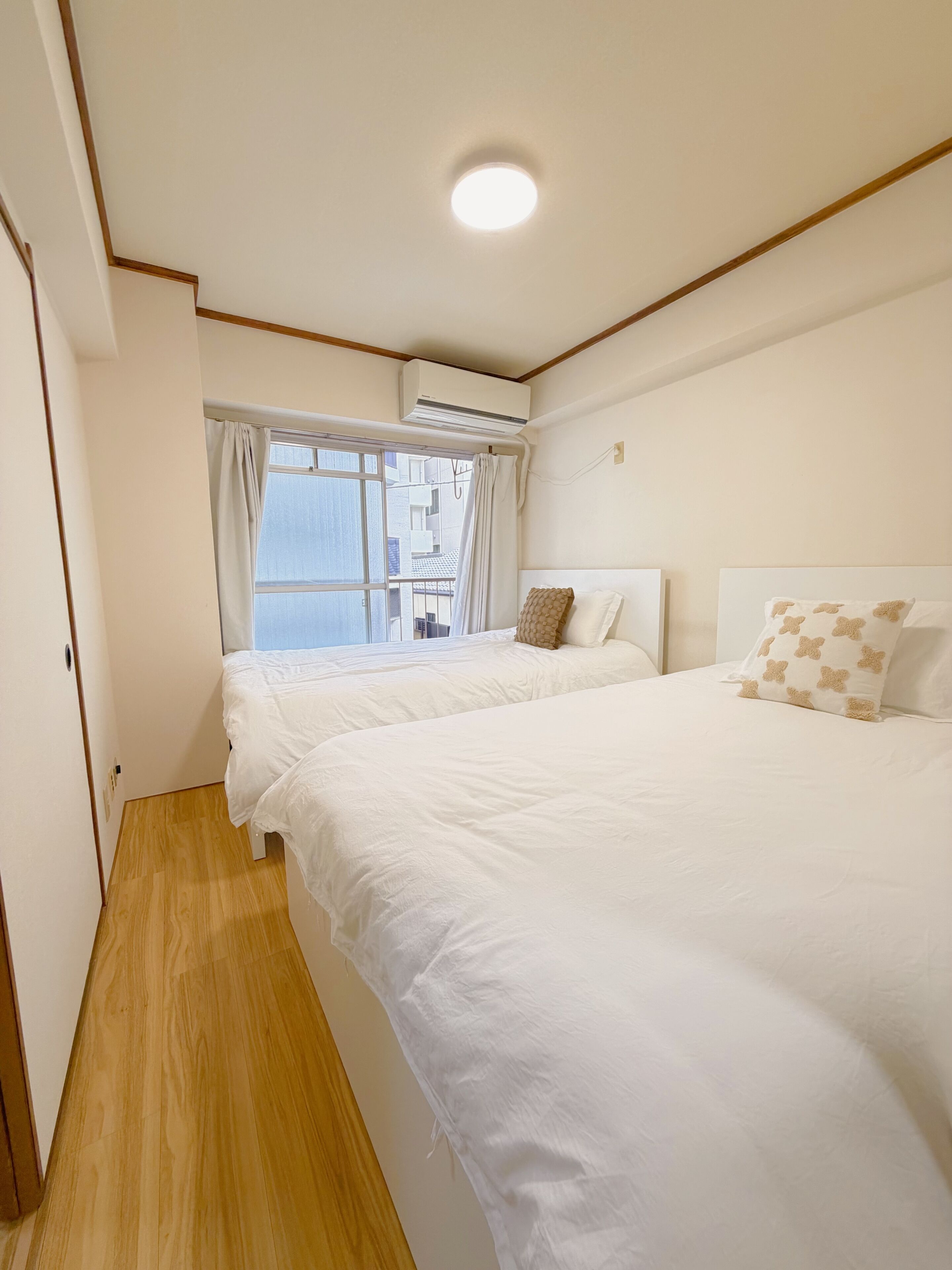Une chambre avec deux lits, une fenêtre avec des rideaux, un appareil de climatisation et un plancher en bois.