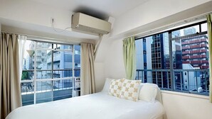 Et hotelværelse med seng, aircondition, store vinduer og udsigt over bybilledet.