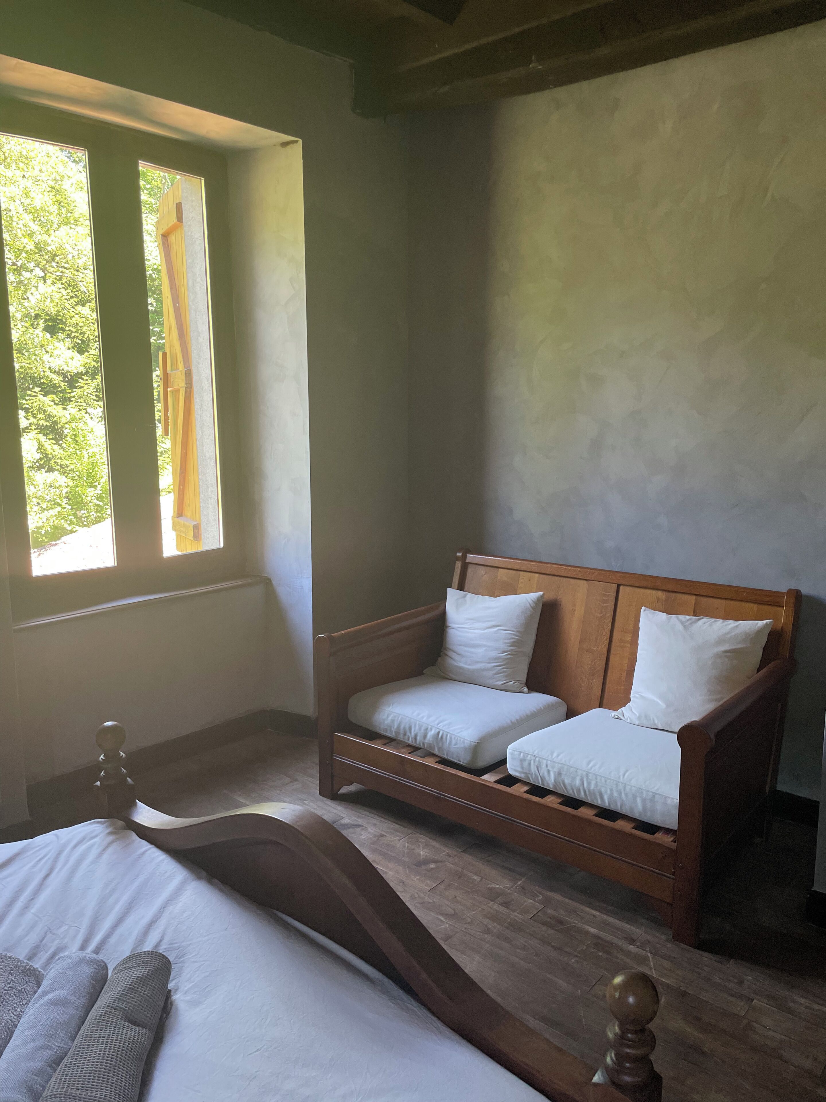 A bedroom with a wooden bed, a wooden bench, and a window with curtains.