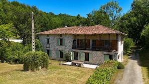 Ein zweigeschossiges Steinhaus mit Ziegeldach und einem Balkon im oberen Stockwerk, sowie einer gepflasterten Auffahrt.
