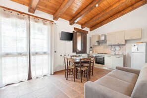 A modern kitchen with wooden beams, a dining area with chairs, a flat-screen TV, and a sofa.