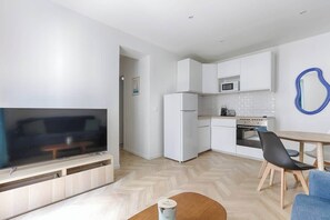Eine moderne Küche mit weißen Schränken, einer Mikrowelle und einem Kühlschrank. Es gibt einen Essbereich mit Tisch und Stühlen.