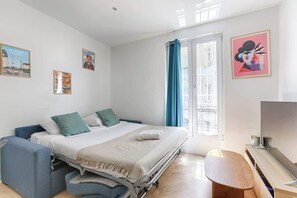 Ein Schlafzimmer mit einem Bett, einem Schreibtisch, einem Fernseher und einem Fenster mit Vorhängen.