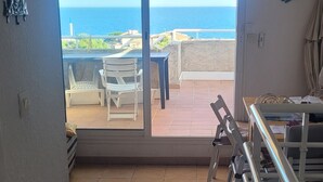 Quarto com vista para o mar, varanda com cadeiras e área de jantar com mesa e cadeiras.