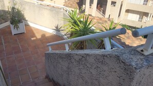 Um terraço com piso de azulejos, plantas em vasos e guarda-corrimão branco.