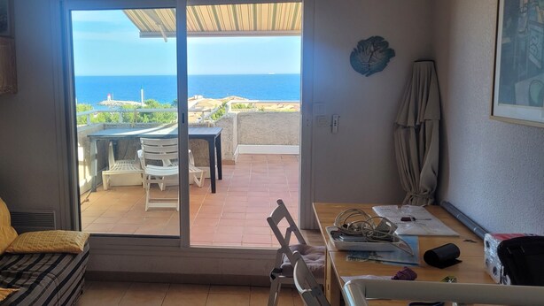 Quarto com porta de vidro deslizante que dá para um alpendre externo com mesa e cadeiras, um sofá com almofadas e um ventilador de teto.