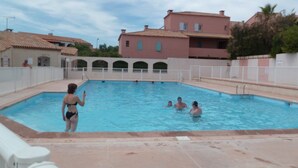 Piscina cercada por uma cerca branca, com pessoas na água.