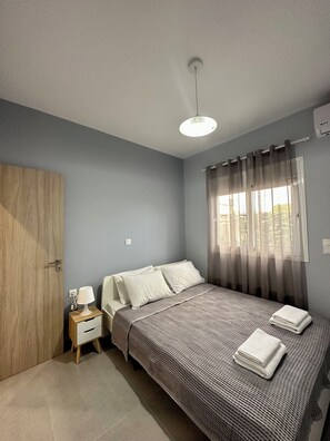A bedroom with a bed, a bedside table with a lamp, a wooden wardrobe, and a window with curtains. - Zouf House Luxury Stay with Jacuzzi (Agios Panteleimon)