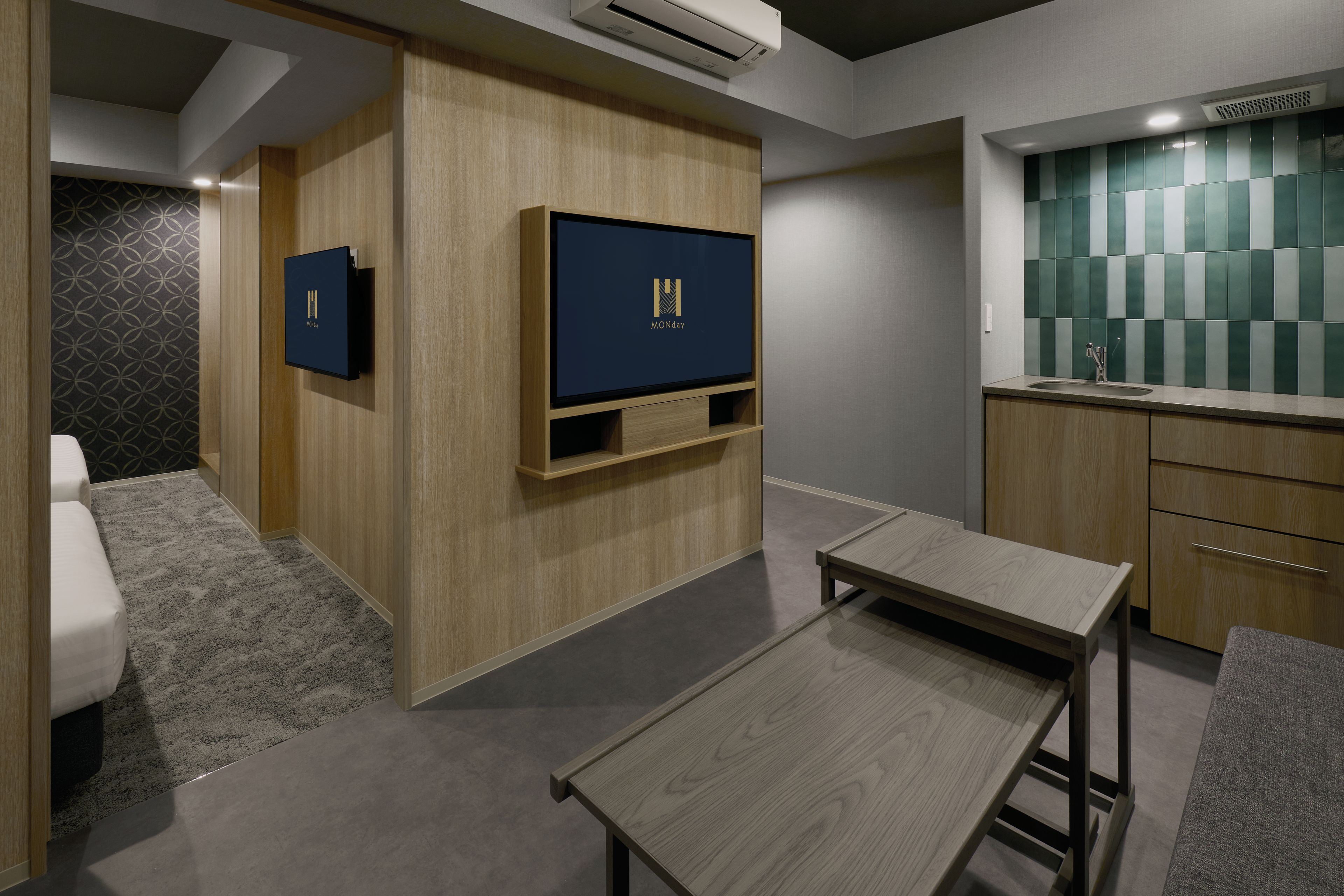Een moderne hotelkamer met een houten wandmeubel, een flatscreen televisie, een klein tafeltje, een bankje en een kitchenette.