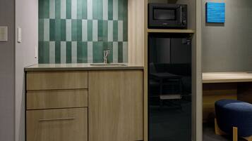 Uma kitchenette compacta com micro-ondas, pia e armário de madeira.