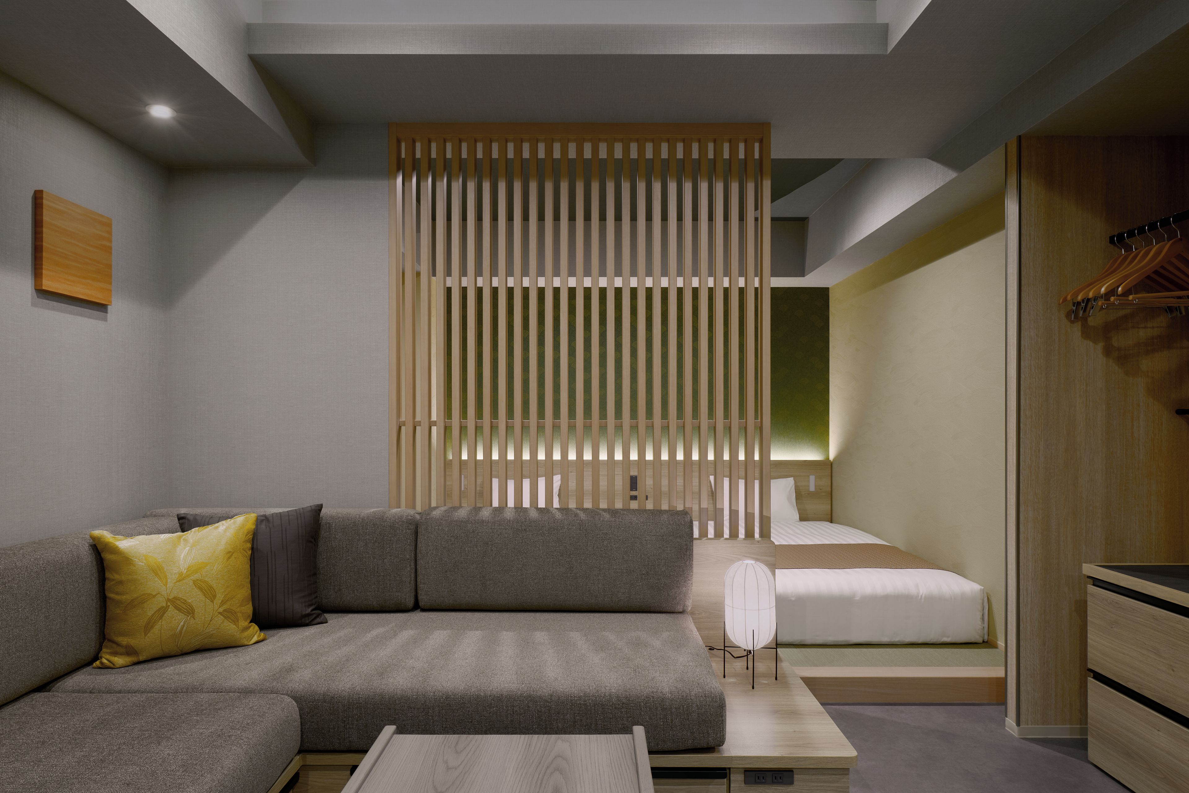 Una habitación de hotel moderna con un sofá gris, un separador de madera, una cama con ropa de cama blanca y un armario de madera.