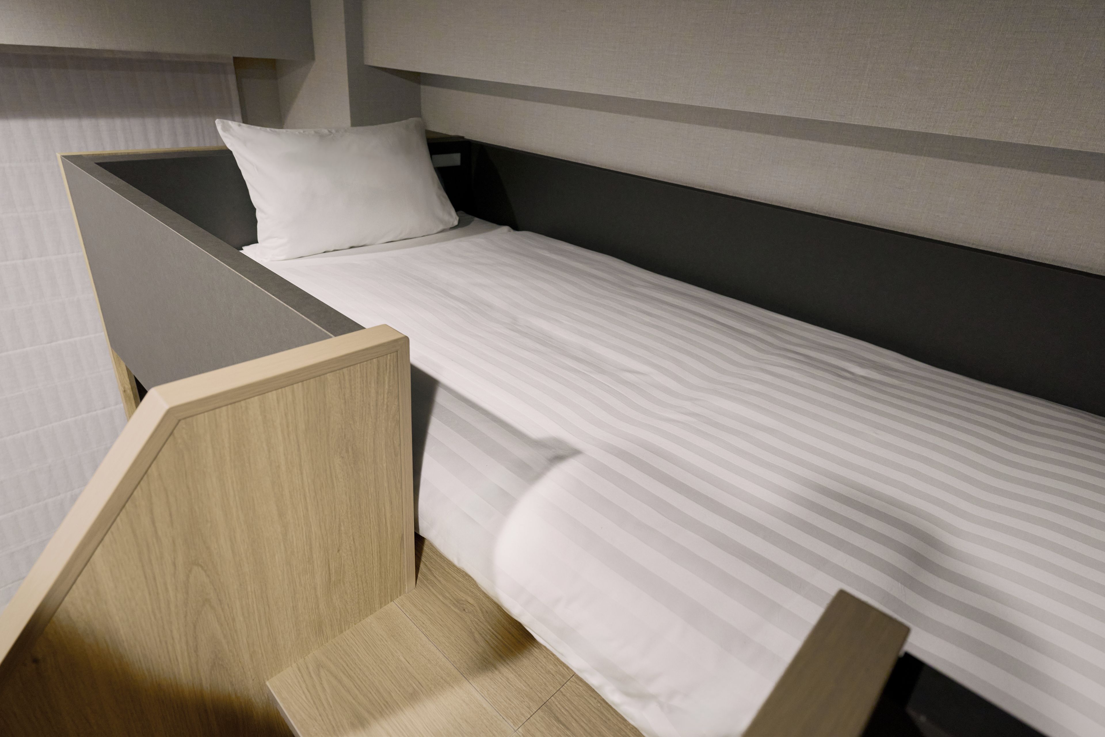 Una cama individual con cabecera de madera y almohada blanca en una habitación con decoración gris y blanca.