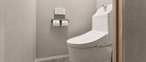 A modern bathroom with a toilet, a paper towel dispenser, and a wall-mounted control panel.