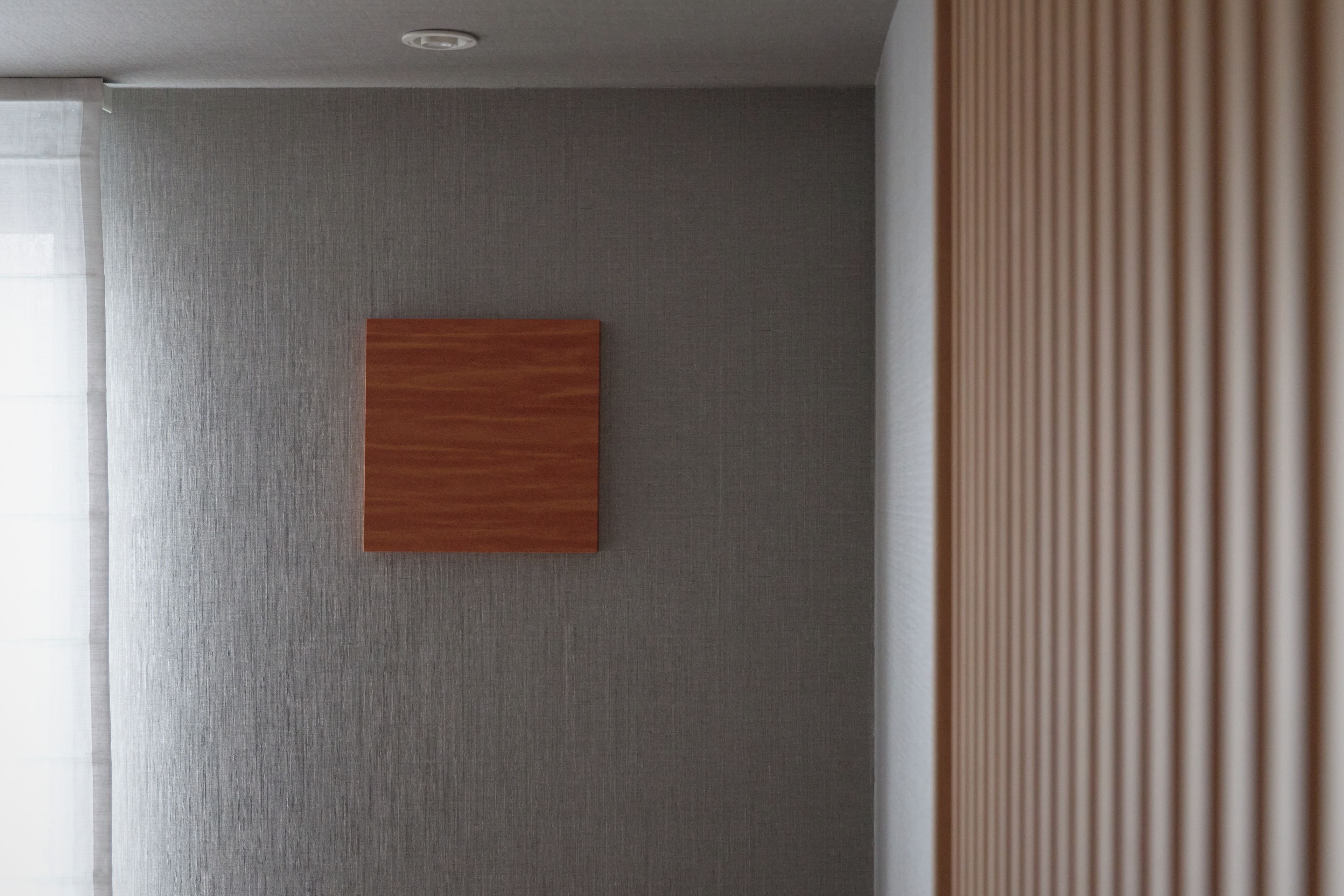 Una habitación con una pared gris con textura, un panel de madera y una ventana con persianas.