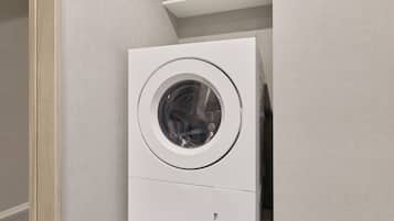 Une machine à laver compacte, blanche, fixée au mur, dotée d’une porte circulaire, et placée dans un coin, contre un mur gris à texture.