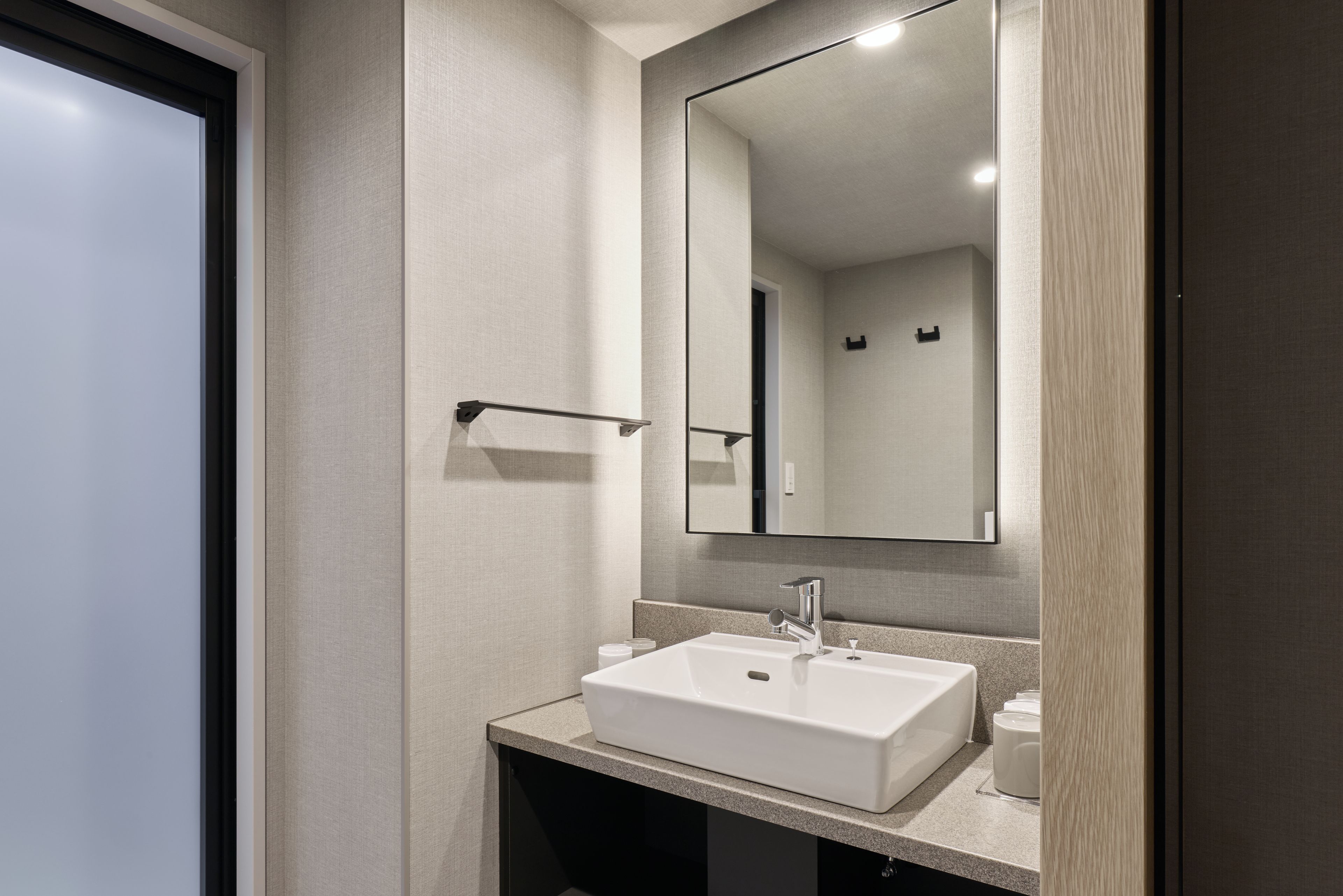 A modern bathroom with a white sink, a large mirror, and a towel rack.