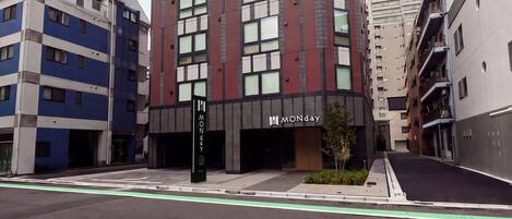 Un edificio de varios pisos con un diseño arquitectónico moderno, que destaca un cartel grande con la palabra 'MONDAY' en la entrada.
