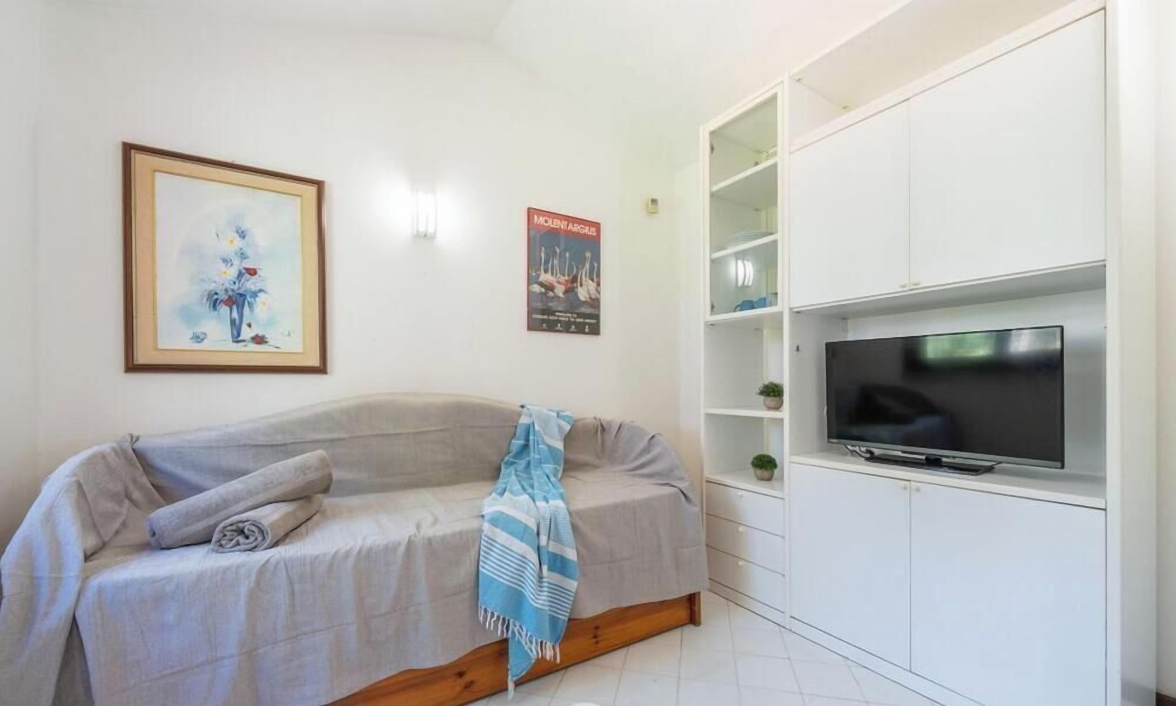 A modern living room with a sofa, a flat-screen TV, and a white cabinet with shelves.