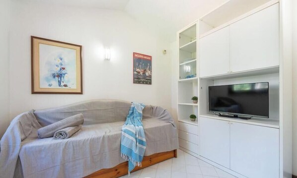 Una sala de estar moderna con un sofá, un televisor de pantalla plana y un mueble blanco con estantes.