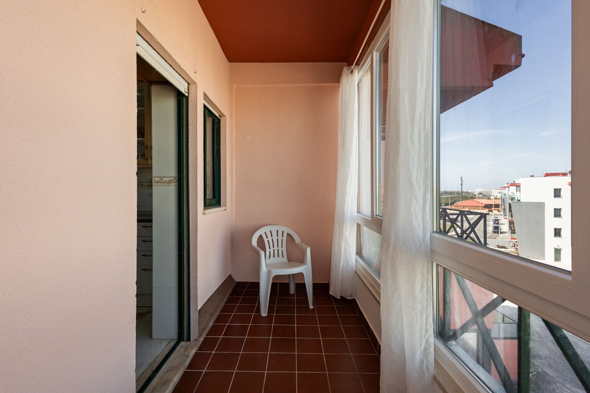 A balcony with a white plastic chair, a tiled floor, and a view of buildings.
