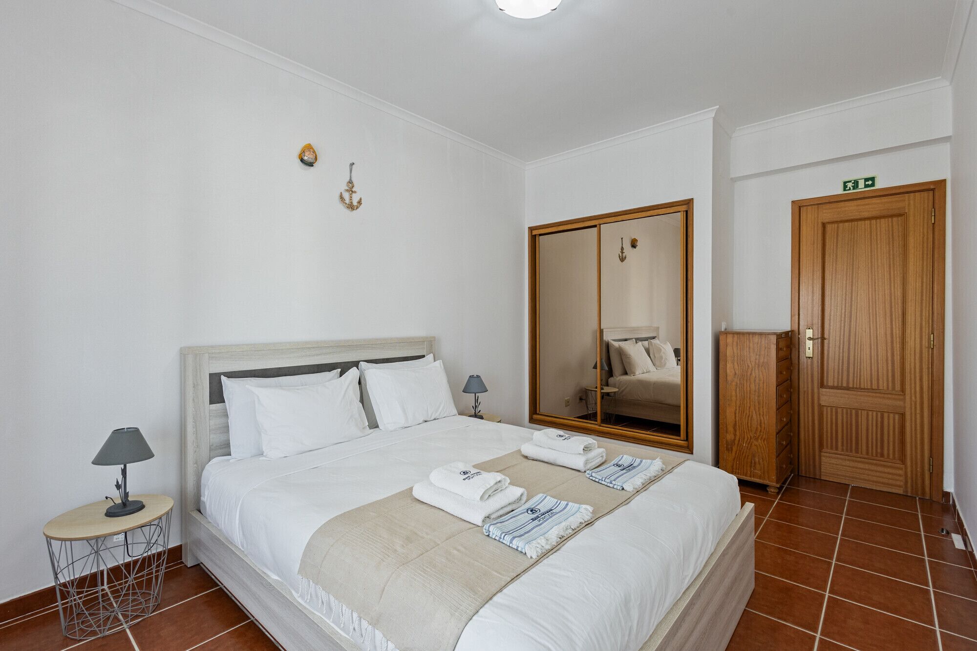 Una habitación de hotel con una cama grande, un armario, una mesita auxiliar y un espejo.