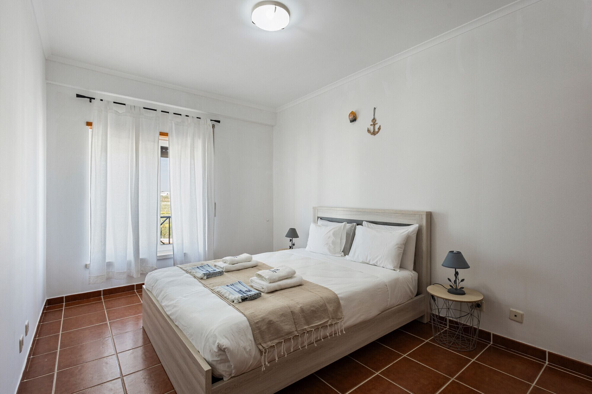 Une chambre à coucher avec un lit, une table de chevet, une lampe et une vue sur l’extérieur.