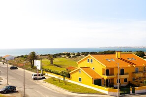 Ein gelbes Gebäude mit rotem Ziegeldach, einem Parkplatz und Blick aufs Meer.