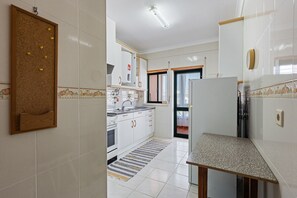 Eine Küche mit weißen Schränken, einem Herd, einem Kühlschrank und einer Korkwand.