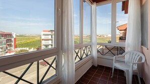 En balkon med udsigt over bygninger og marker, en stol og et gelænder.