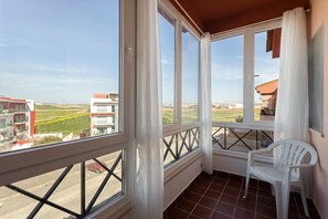 Ein Balkon mit Blick auf Gebäude und Felder, ein Stuhl und ein Geländer.