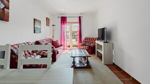 En stue med sofa, sofabord, fjernsyn og balkon med røde gardiner.