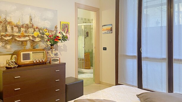 A bedroom with a bed, a dresser, a radio, and a painting. - Riflesso del Lario by Interhome (Bellano)