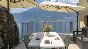 A terrace with a table, chairs, and umbrellas overlooking a lake and mountains. - Riflesso del Lario by Interhome (Bellano)