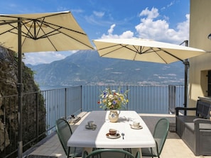 A terrace with a table, chairs, and umbrellas overlooking a lake and mountains. - Riflesso del Lario by Interhome (Bellano)