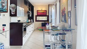 A modern kitchen with a dining area, featuring a glass table, a built-in oven, and a large clock. - Riflesso del Lario by Interhome (Bellano)